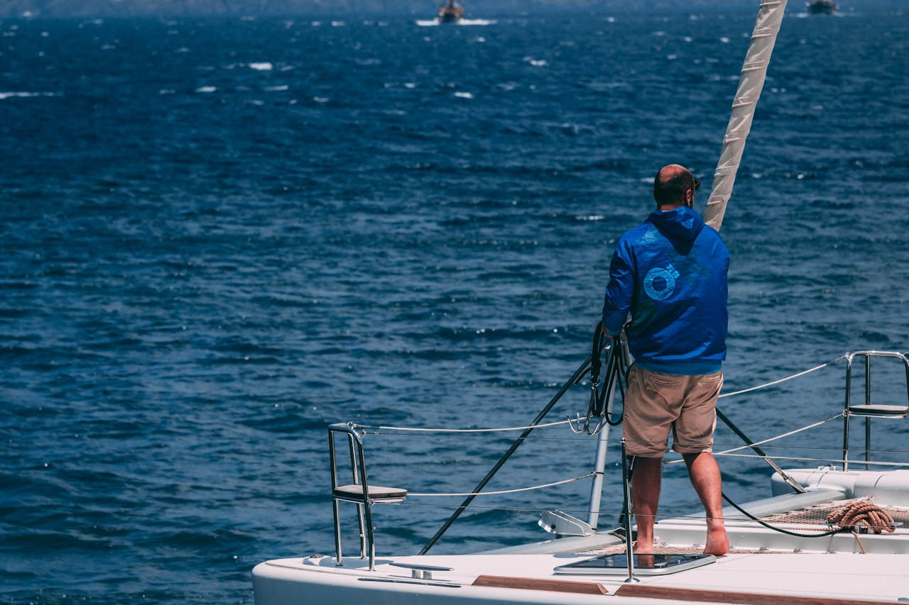 creative-03 A man stands on a yacht deck, navigating the tranquil ocean on a clear summer day.