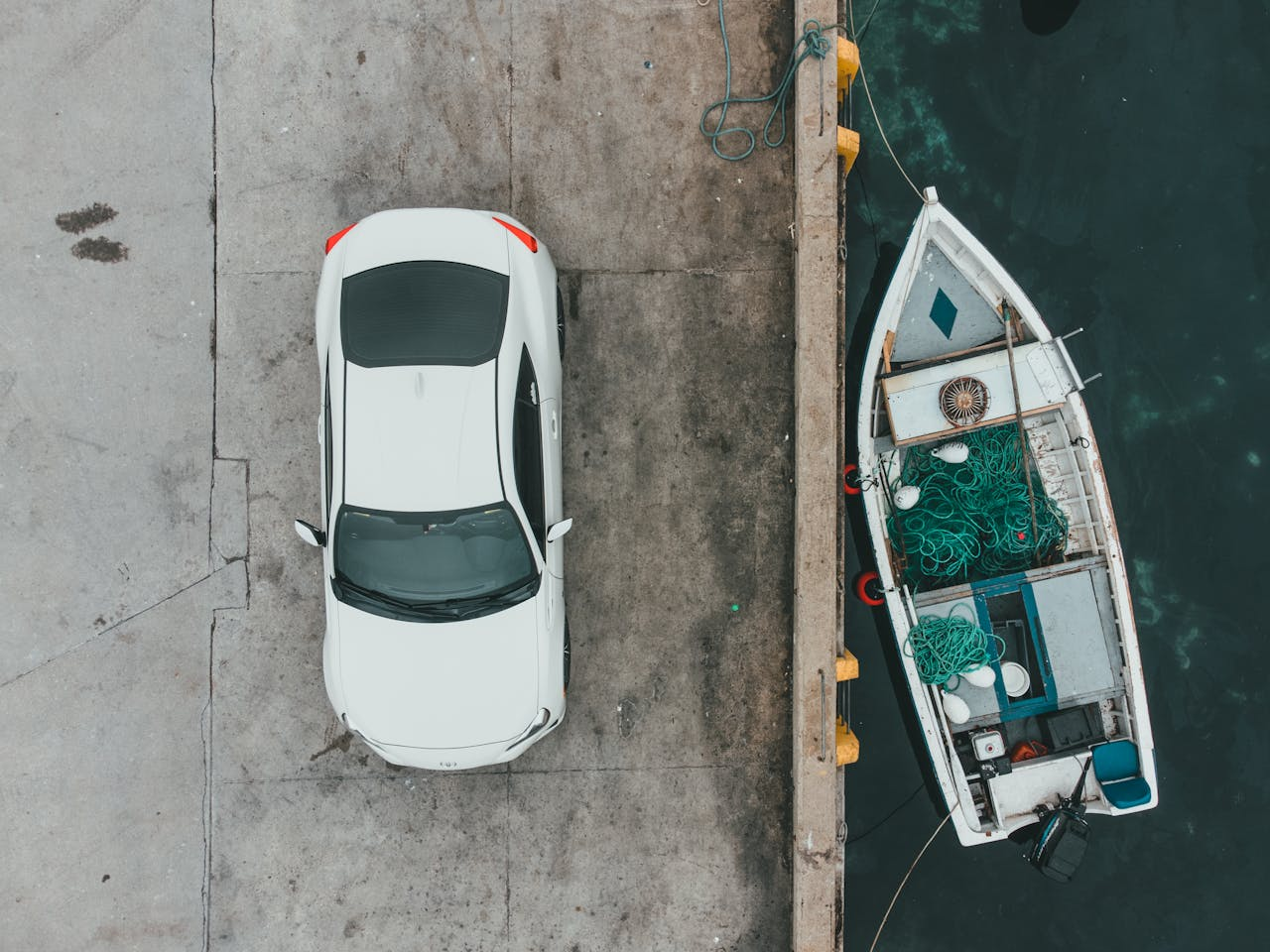 digital-01 Aerial view of a white car parked next to a boat at the dock, captured during the day.